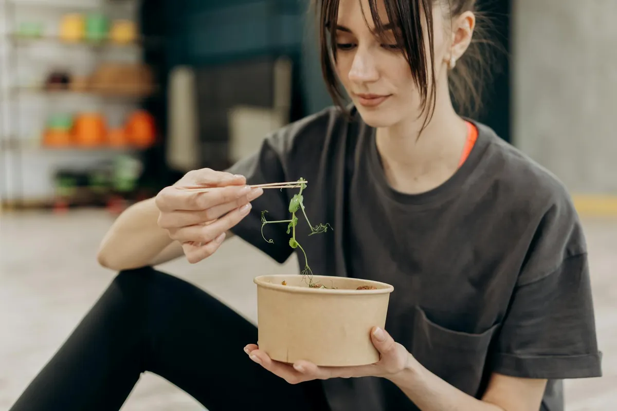 Woman smiling while enjoying a colorful, healthy salad at her kitchen table, demonstrating mindful eating.
