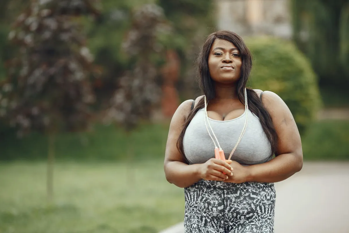 A smiling woman walking briskly on a scenic park path, looking determined and healthy.