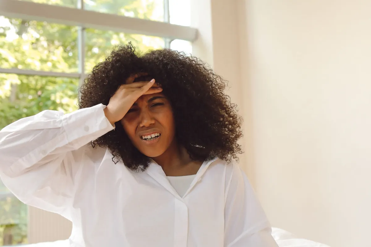 Woman looking concerned while holding her head, symbolizing confusion between aging and vitamin deficiency.