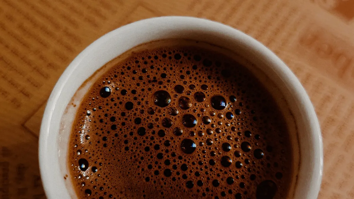 A steaming mug of coffee with abstract cellular patterns in the background, symbolizing the connection between coffee consumption and cellular health for youth and stress resilience.