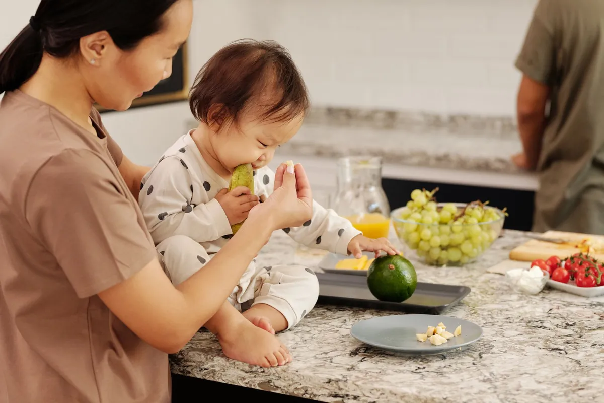 Parent showing a toddler a plate of colorful, whole fruits and vegetables.