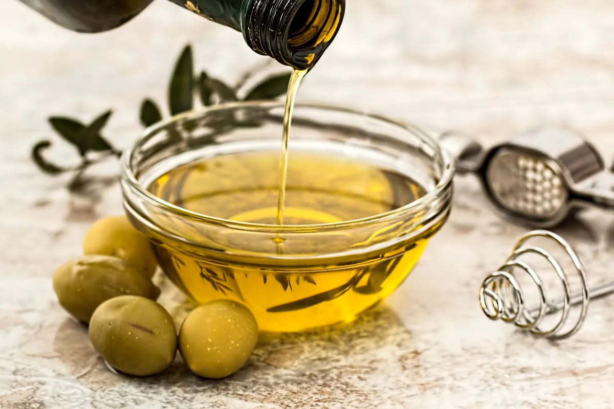 A bottle of Extra Virgin Olive Oil next to a small bowl of olives on a rustic wooden surface.