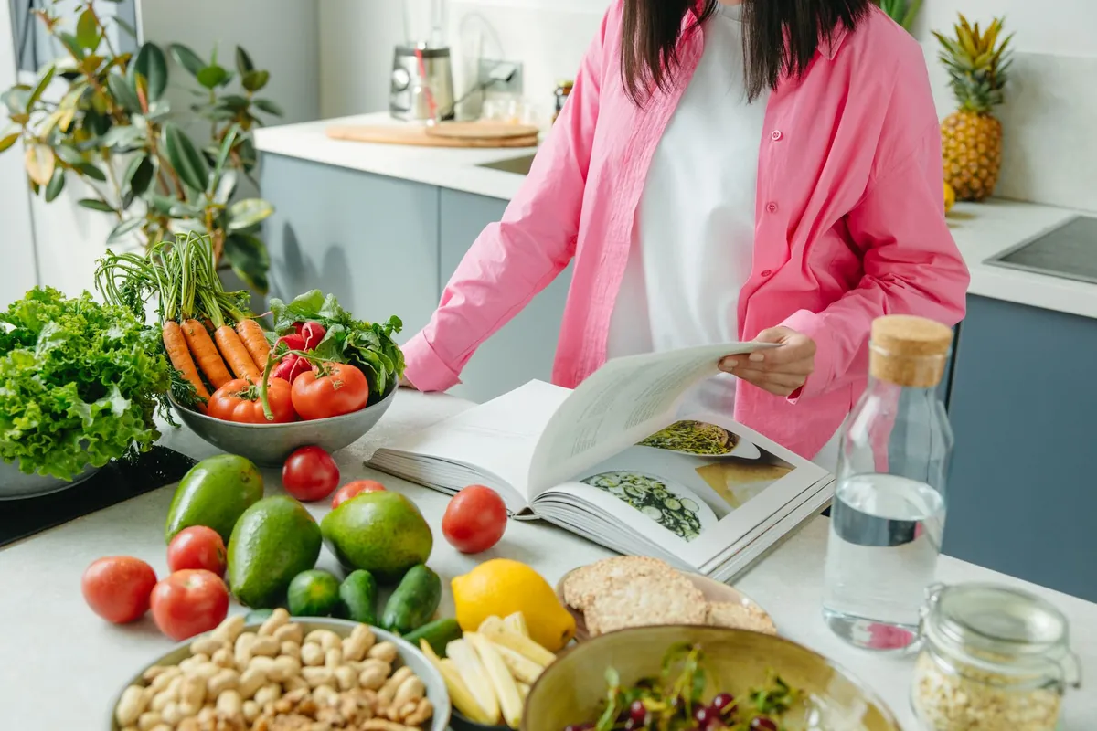 A smiling woman is enjoying a large, vibrant vegan salad filled with fresh vegetables and beans, demonstrating a satisfying low-fat vegan meal for weight loss.