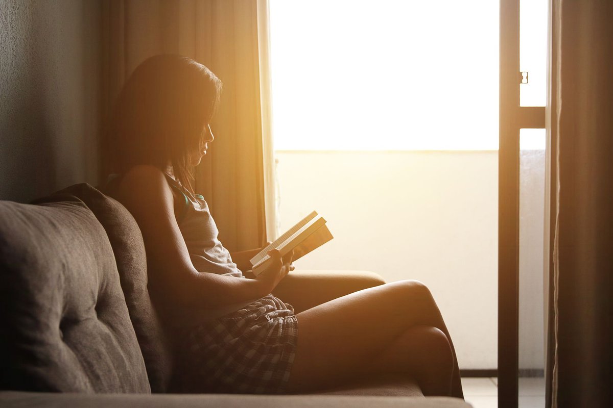 A person enjoying warm sunlight indoors while reading, representing vitamin D absorption and pain relief.