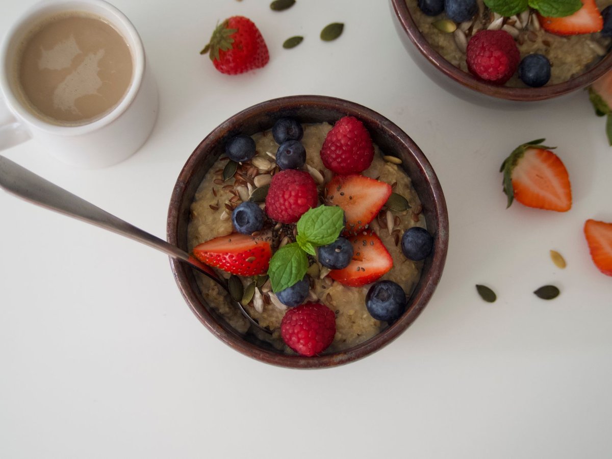 A healthy bowl of oatmeal topped with fresh berries and seeds on a wooden table.