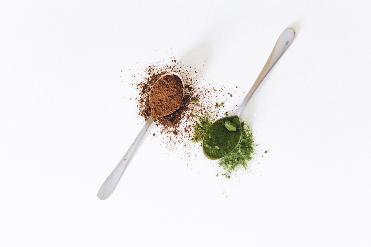 A clean glass of water beside a measuring spoon with white creatine powder on a wooden table.
