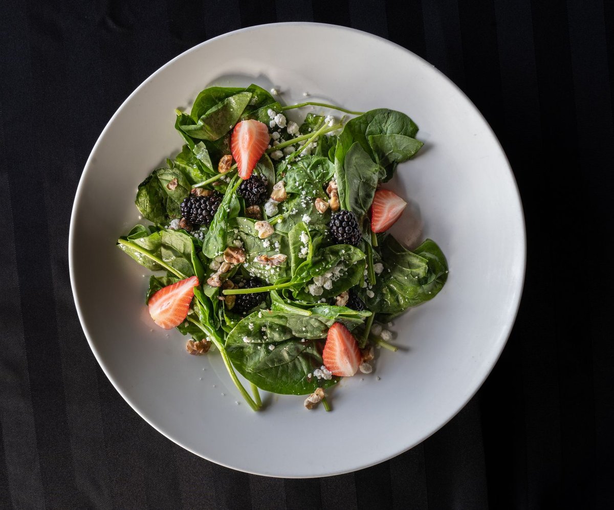 Fresh blueberries and dark leafy greens arranged neatly on a wooden table representing brain food.