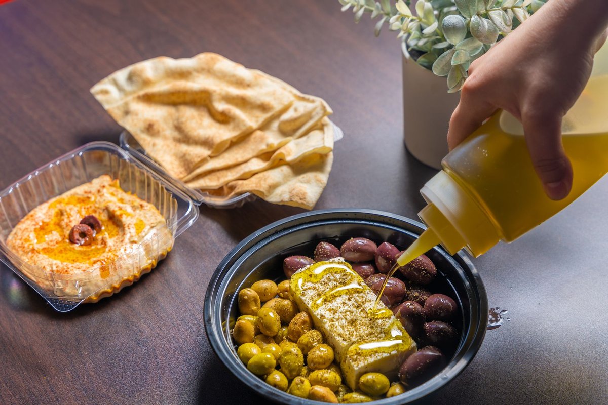 A bottle of extra virgin olive oil being poured into a small dipping dish beside crusty bread