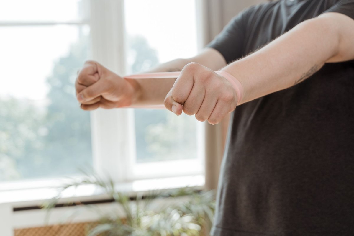 A person in athletic wear doing gentle recovery exercises using a resistance band inside a bright home gym.